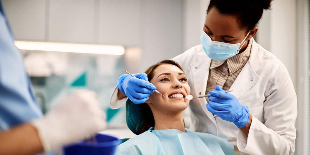 دندانپزشک در حال معاینه دندان‌های بیمار روی یونیت